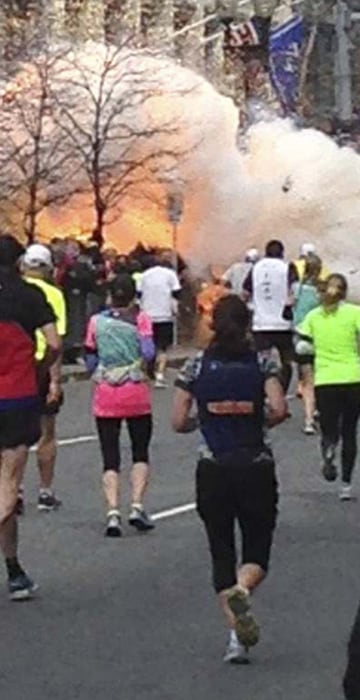 Image: Runners continue to run towards the finish line as an explosion erupts at the finish line of the Boston Marathon